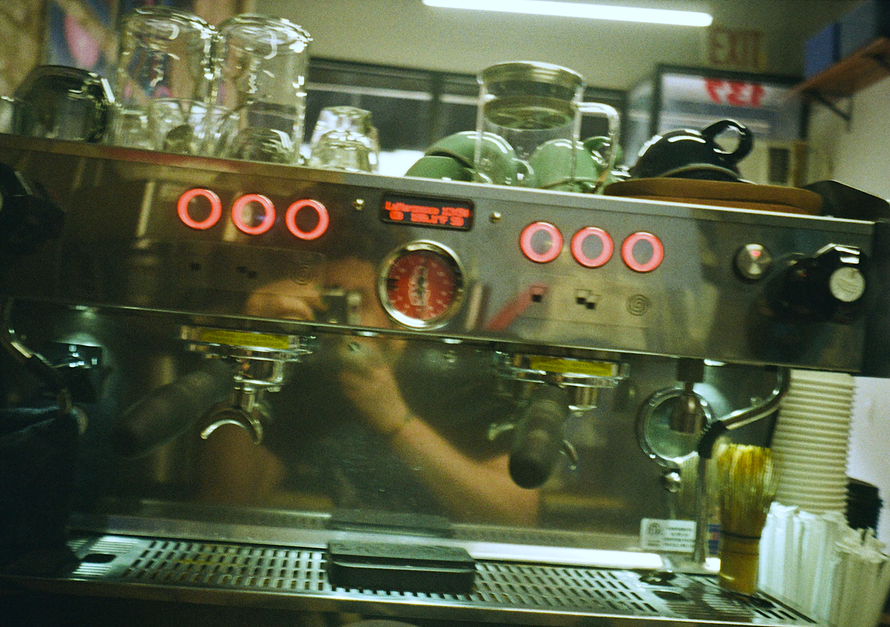 A selfie with a film camera taken from the reflection of the espresso machine.